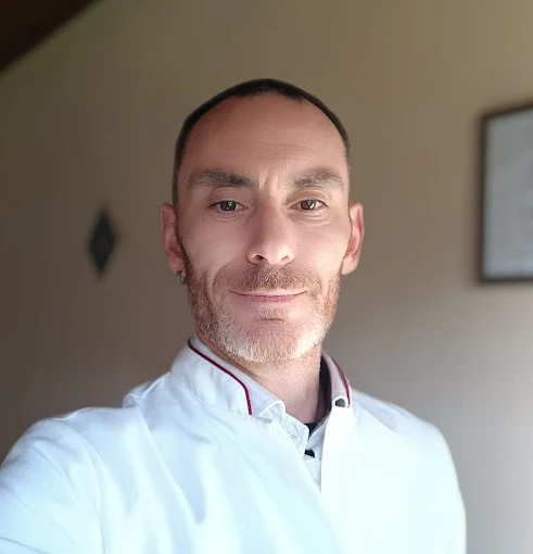 Imagem do terapeuta Rodrigo Cainelli utilizando uma camisa estilo bata indiana na cor branca com a mão esquerda tocando o centro do peito.